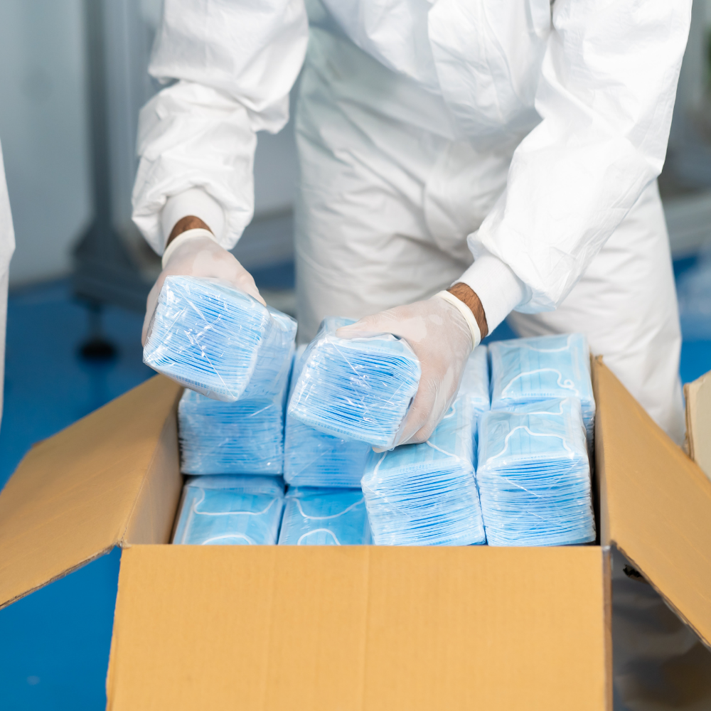 Person dressed in PPE packing surgical masks into a shipping box
