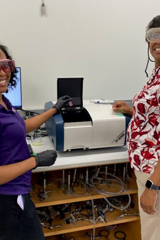 Two women standing at a laboratory bench facing backward toward camera smiling.