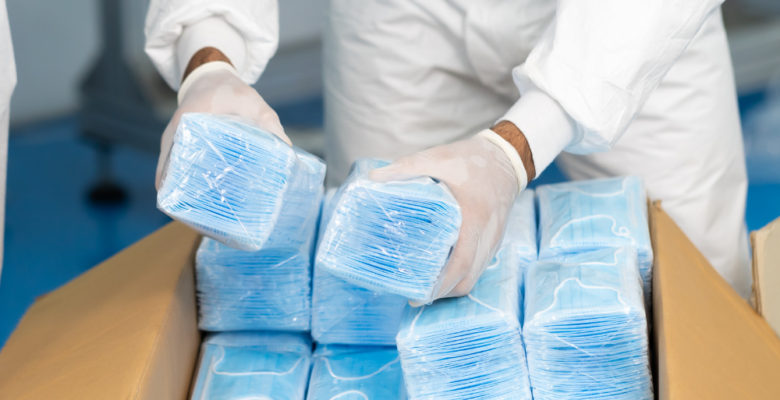 Person dressed in PPE packing surgical masks into a shipping box