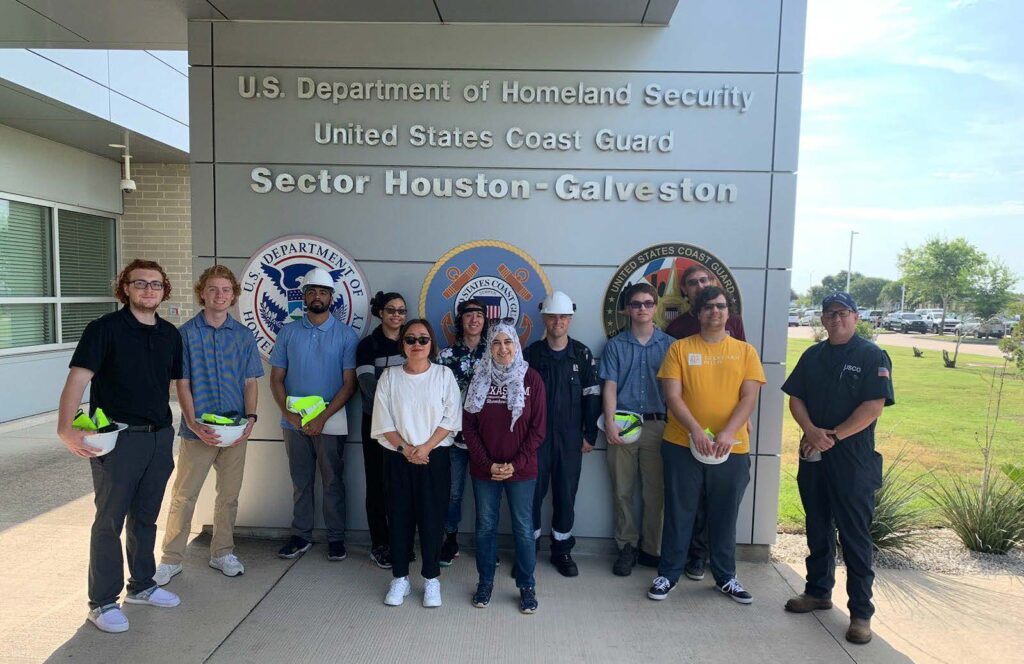 Students in a group posing for a picture in front of a U.S. DHS and Coast Guard sign with a member of the Coast Guard in Galveston