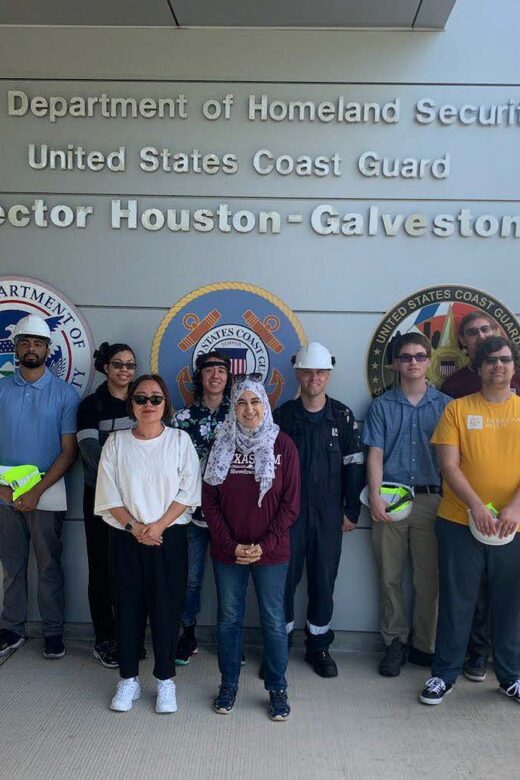 Students in a group posing for a picture in front of a U.S. DHS and Coast Guard sign with a member of the Coast Guard in Galveston